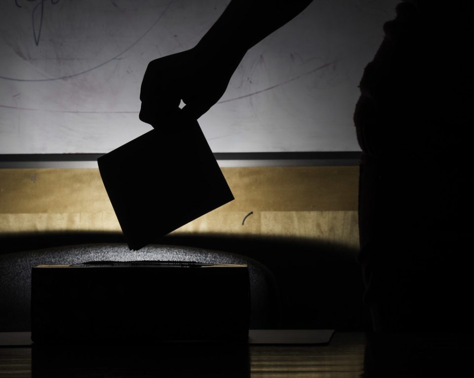 silhouette of a person placing a polling card into a ballot box