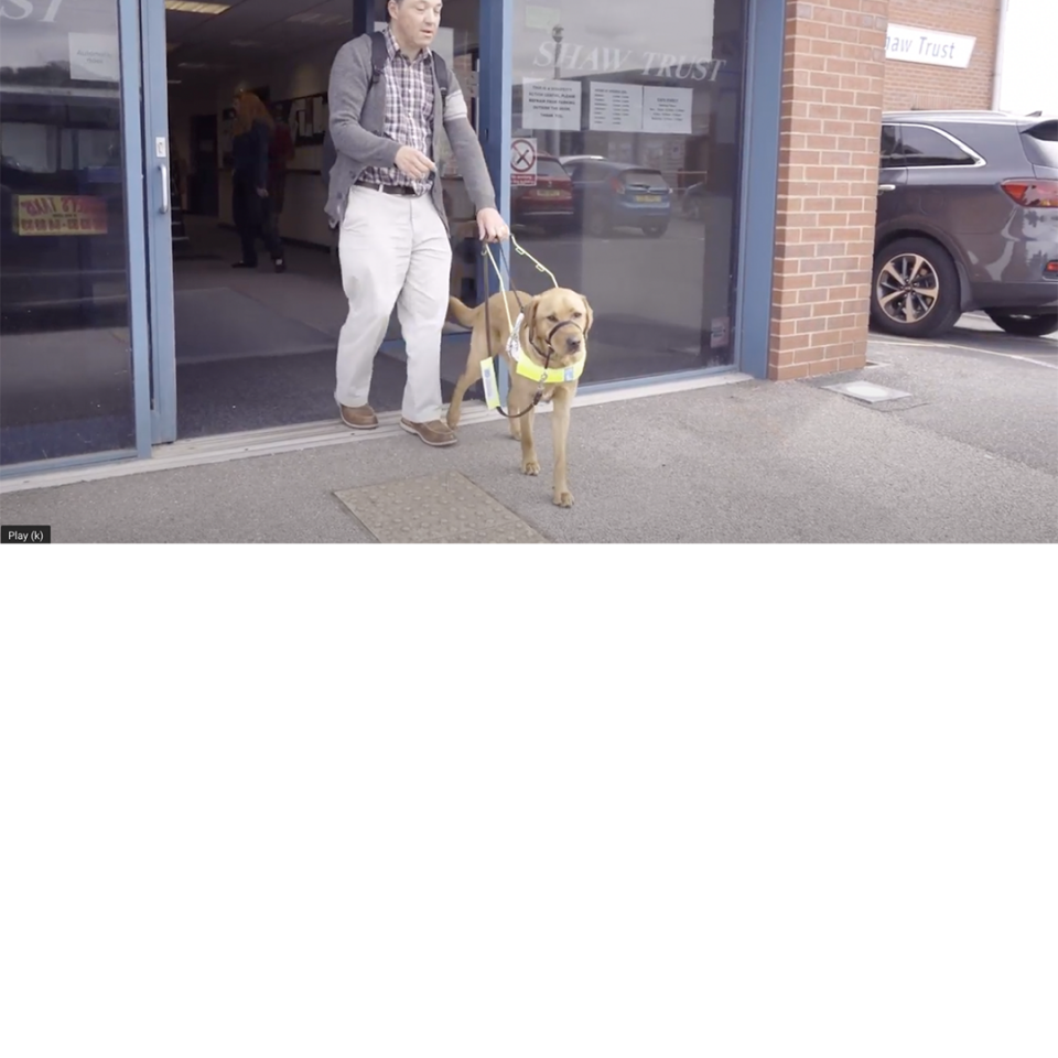 Alan Sleat walking out of the Shaw Trust building with his service dog, who is a sandy coloured labrador