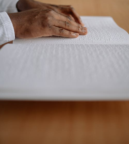 a Black man's hands reading braille from a book