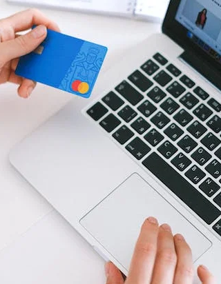 someone holding a credit card in one hand, whilst using a laptop with the other