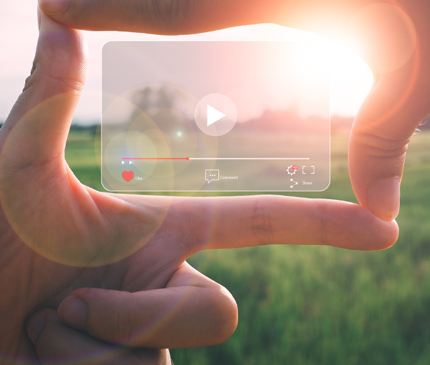 an outdoor sunny field has a media player overlaid on top of it, with someone's hands encompassing the player with their fingers like they are framing a shot.